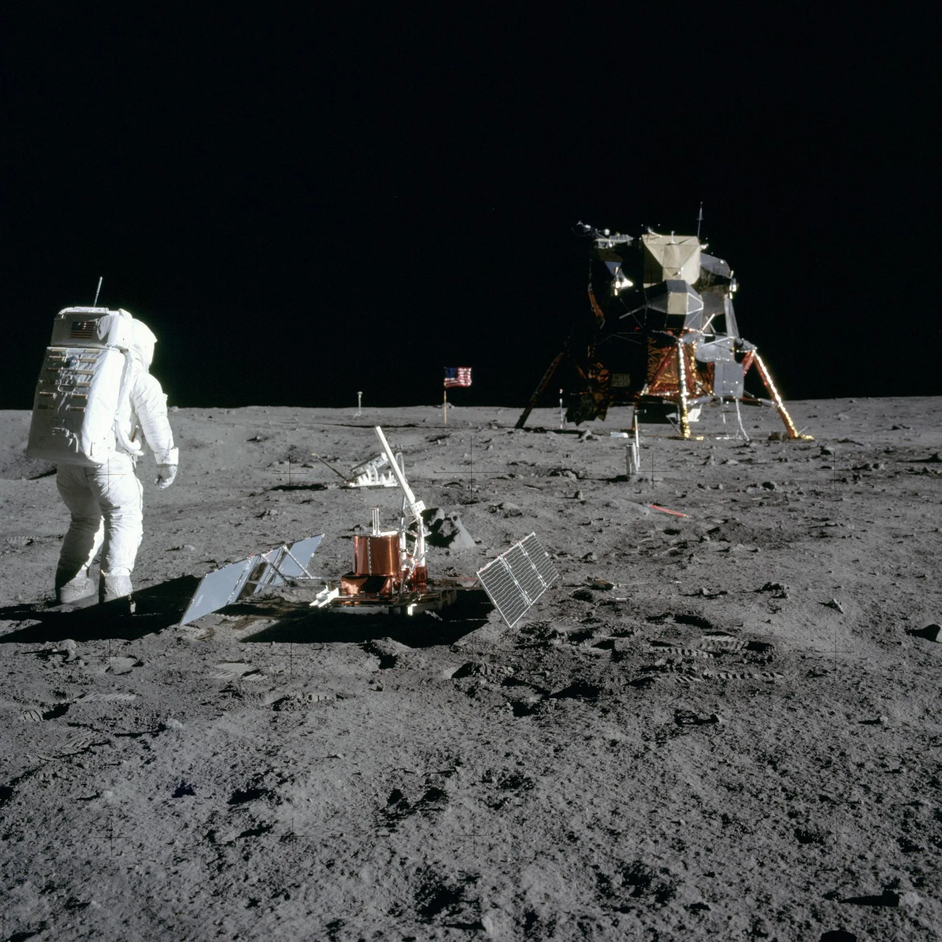 Apollo 11'in Ay yüzeyinde kurduğu deney paketi: önde sismometre, onun ardında lazer yansıtıcısı, arka planda bayrak ve sağda Ay modülü Eagle. Fotoğrafı Neil Armstrong çekti, 20 Temmuz 1969.