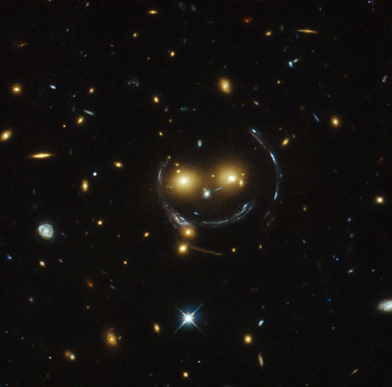 Gülen yüz: SDSS J1038+4849 gökada kümesinin kütleçekimi, arkadaki gökadaların ışığını yaylara dönüştürerek bir 'gülümseme' oluşturuyor. Hubble görüntüsü.