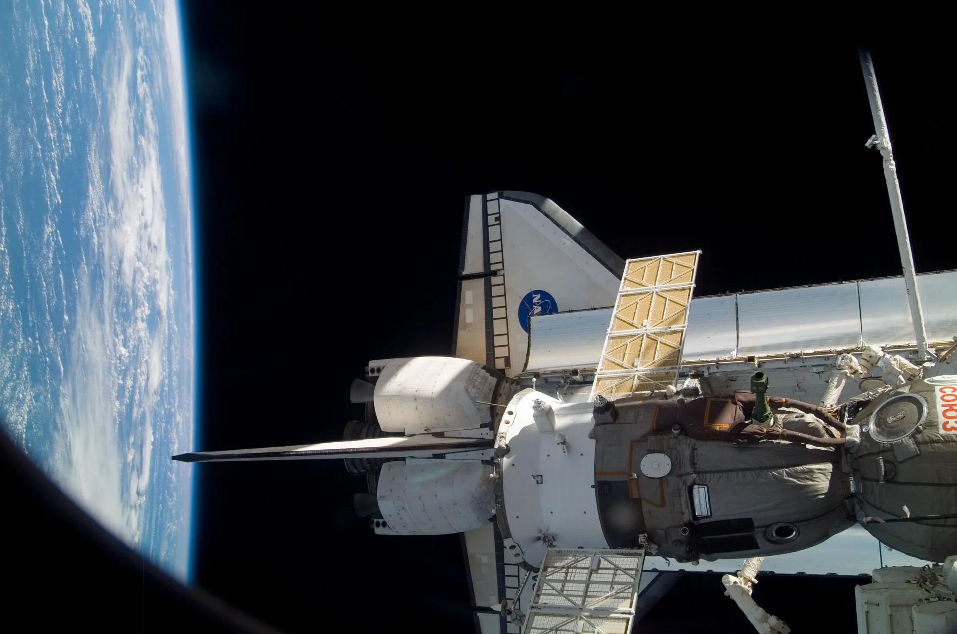 Uluslararası Uzay İstasyonu'na kenetlenmiş Discovery mekiği ve bir Soyuz aracı, arkada Dünya'nın ufku (26 Ekim 2007)